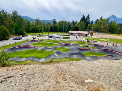 Paved pump track at Enchantment Park with the parking lot and restrooms behind it